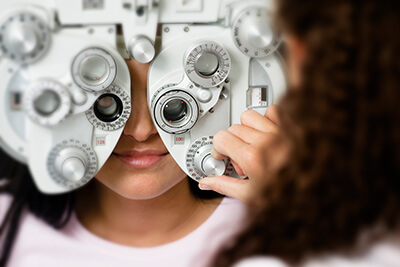 A close up shot of a person getting their eyes checked on a machine, with an optician adjusting knobs on the machine