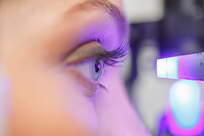 Side view of a woman's face with a glaucoma test machine very close to her eye, shining into it, and giving off a purple glow.