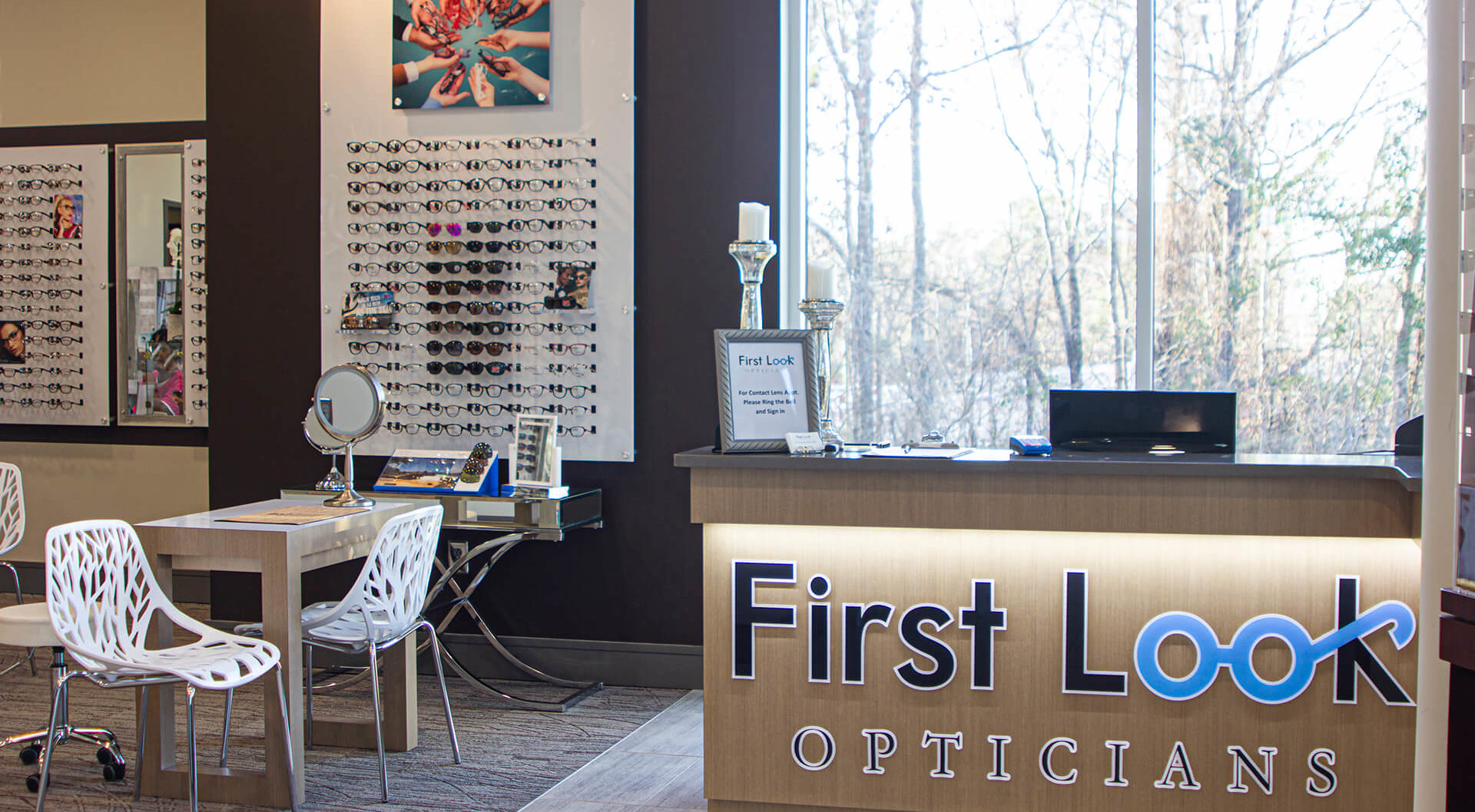 View of the FIrst Look Opticians front desk, well lit room, glasses selection all along the walls, small desks for meeting with the opticians.