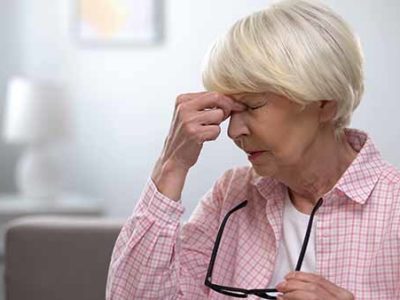 Aged woman taking off eyeglasses and massaging painful nose, migraine pain