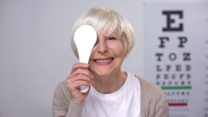 Retired female closing eye and smiling to camera, successful cataract surgery