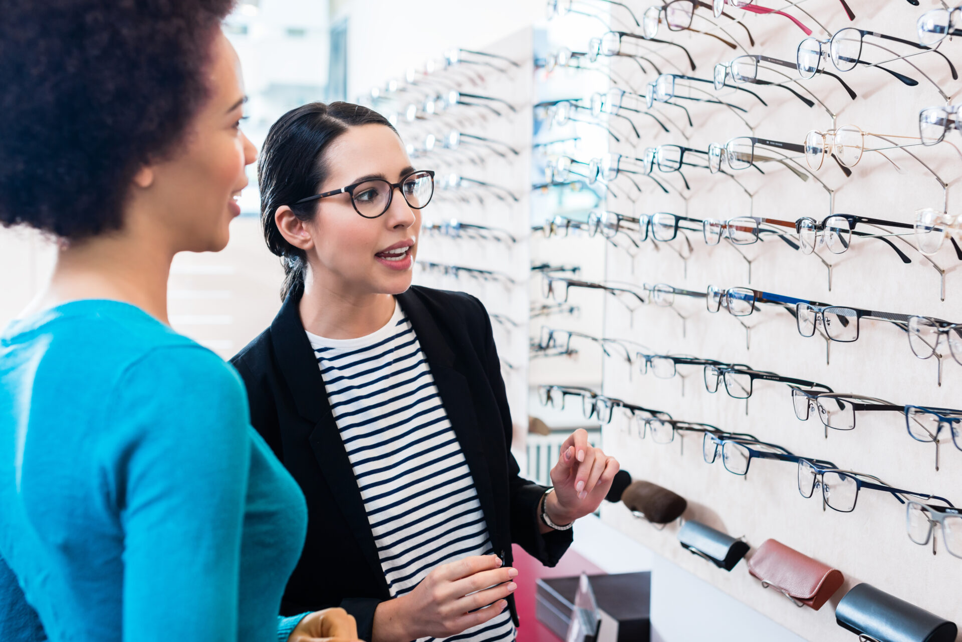 Cheerful black woman inspecting glasses in an optical shop with help from an optician
